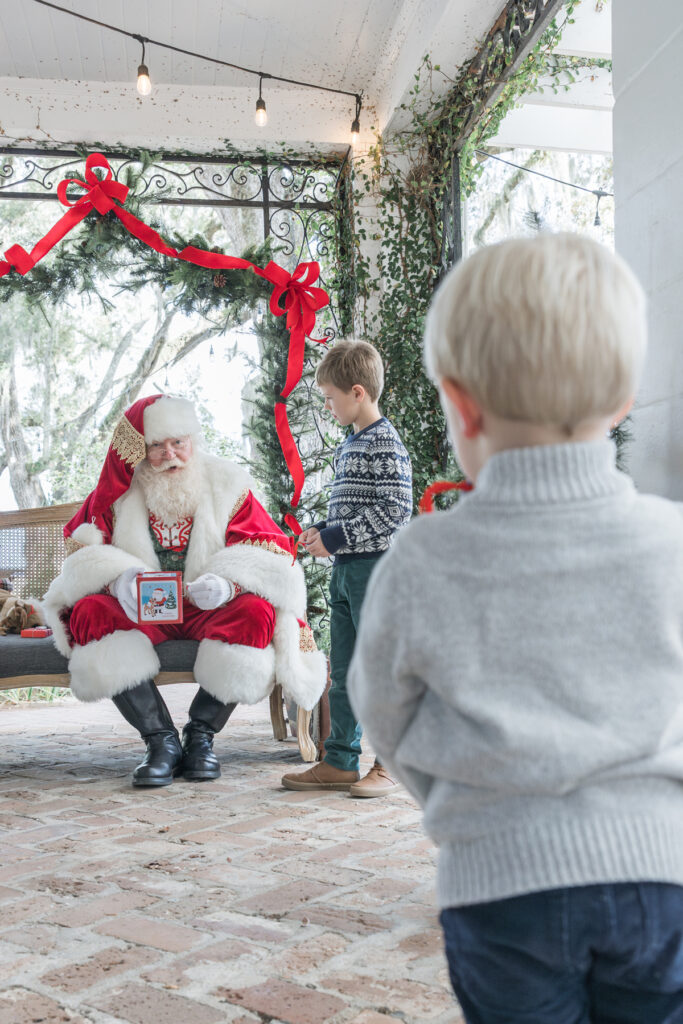 A younger brother looks on as his older brother talks to Santa at a portrait event in Savannah.