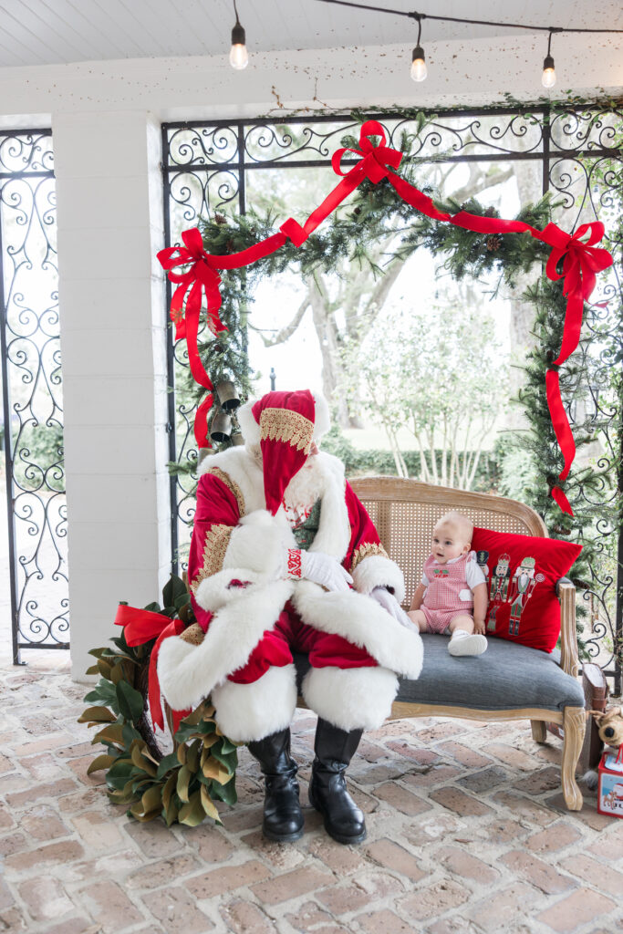 A one year old baby boy sits in awe of Santa, who is sitting on a bench with him.