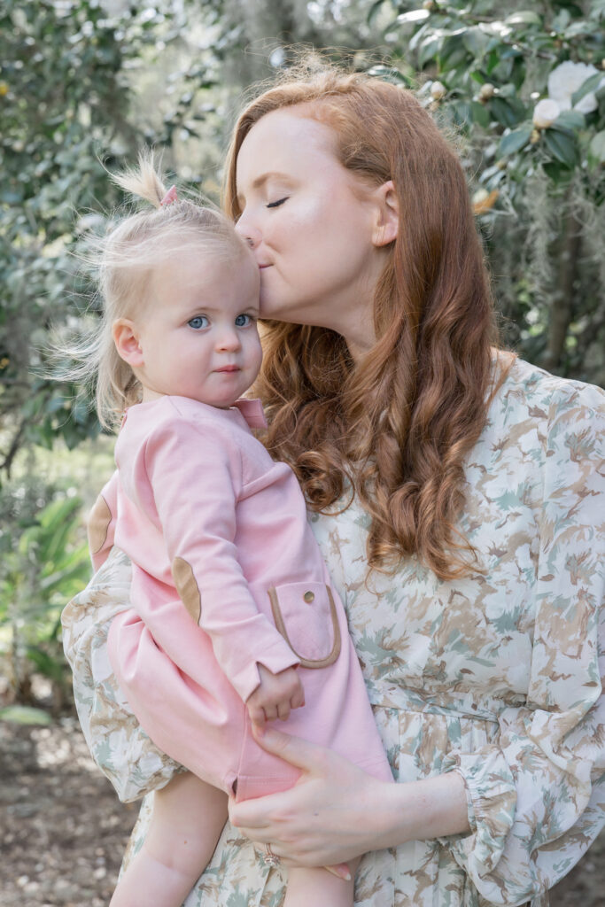 A mom kisses her daughter on the temple in a garden of camellia flowers in Savannah.