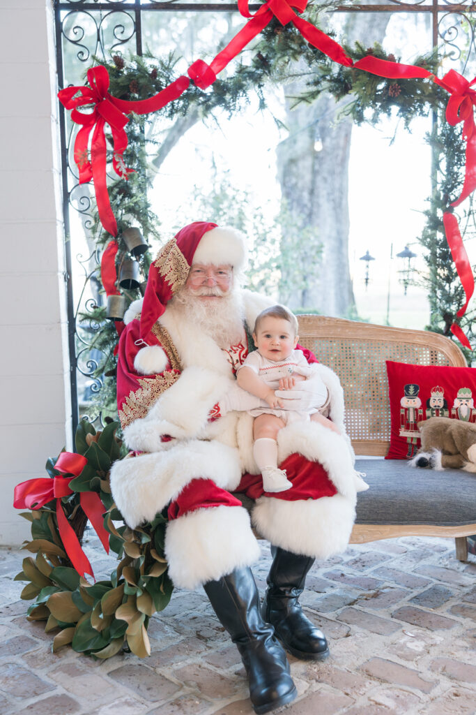 A seven month old baby boy, dressed in a Feltman Brothers holiday bubble, sits on Santa's lap and smiles at HollyOaks on the Marsh in Savannah, Georgia.