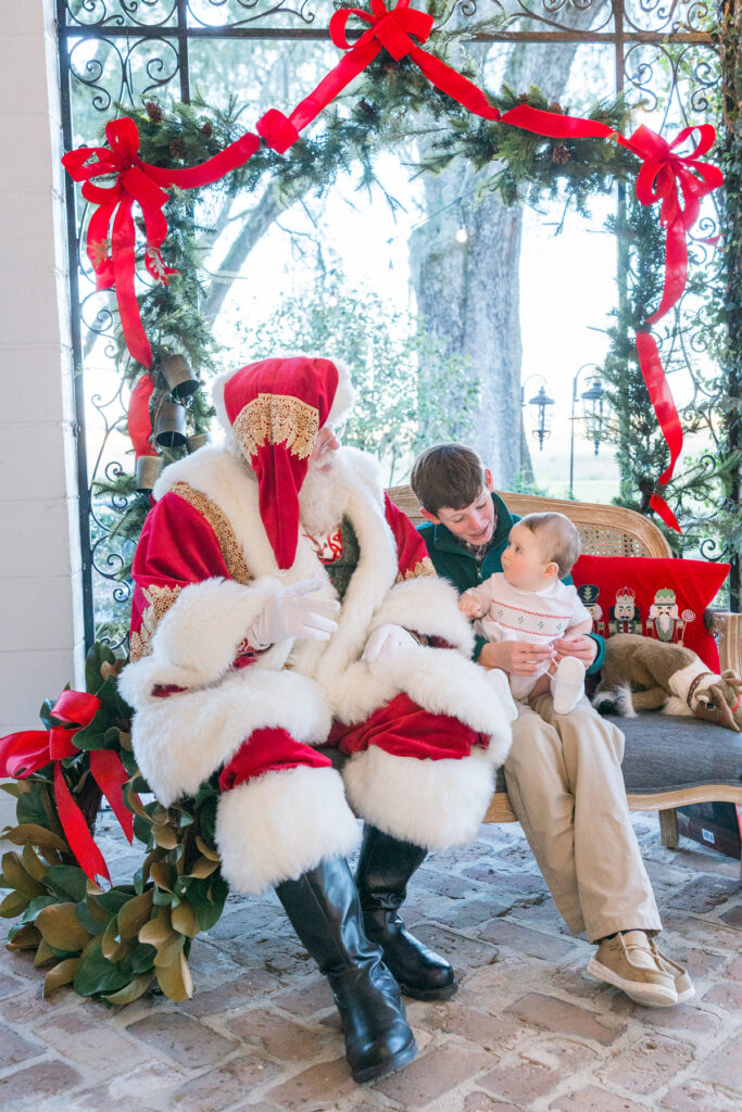 Santa, an older brother, and baby brother sitting on a bench in Savannah, Georgia with live oaks in the background.