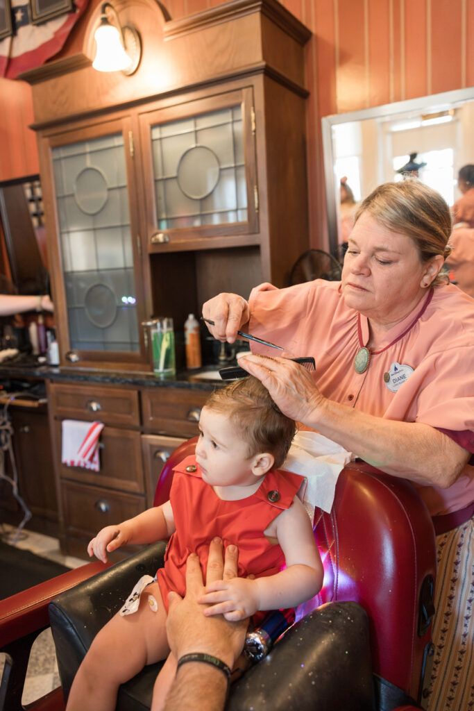 A little boy in a red Beaufort Bonnet jon jon gets his first haircut in Disney