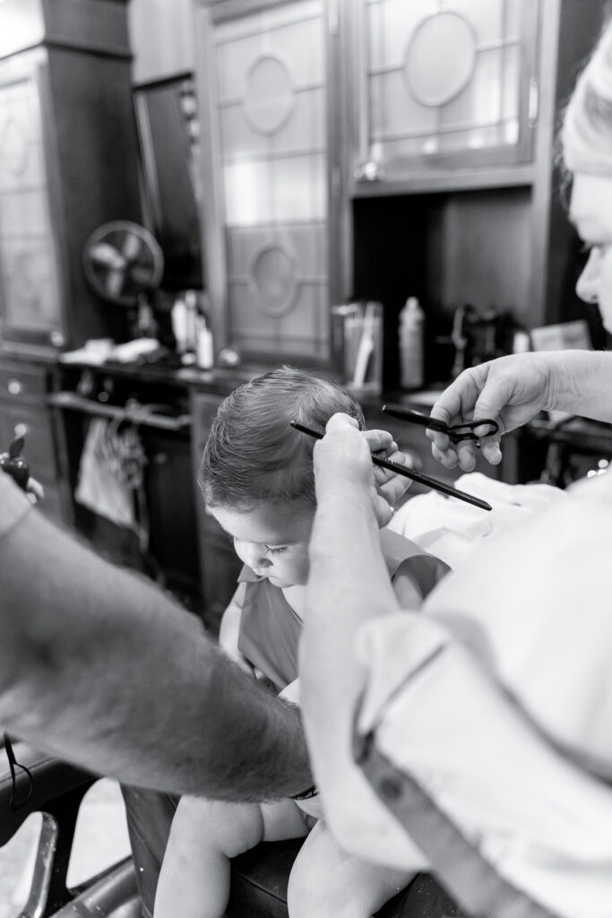 A black and white image of a lady cutting a toddler's hair.