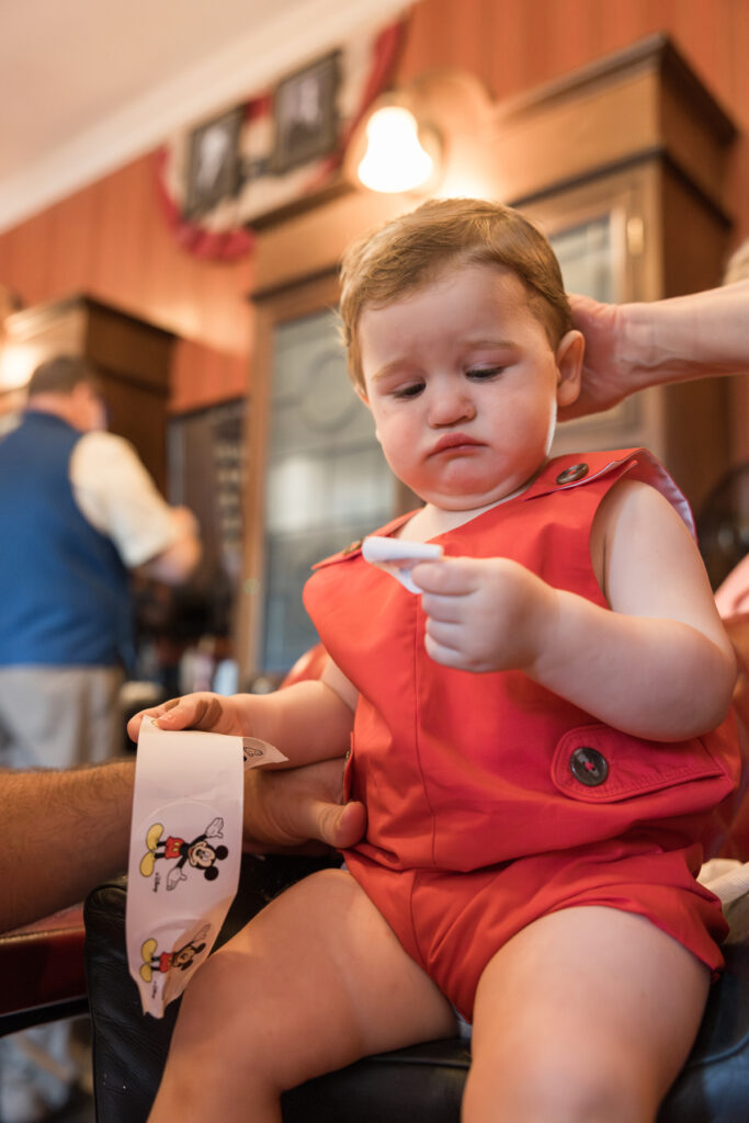 A frowning toddler examines a Mickey Mouse sticker.