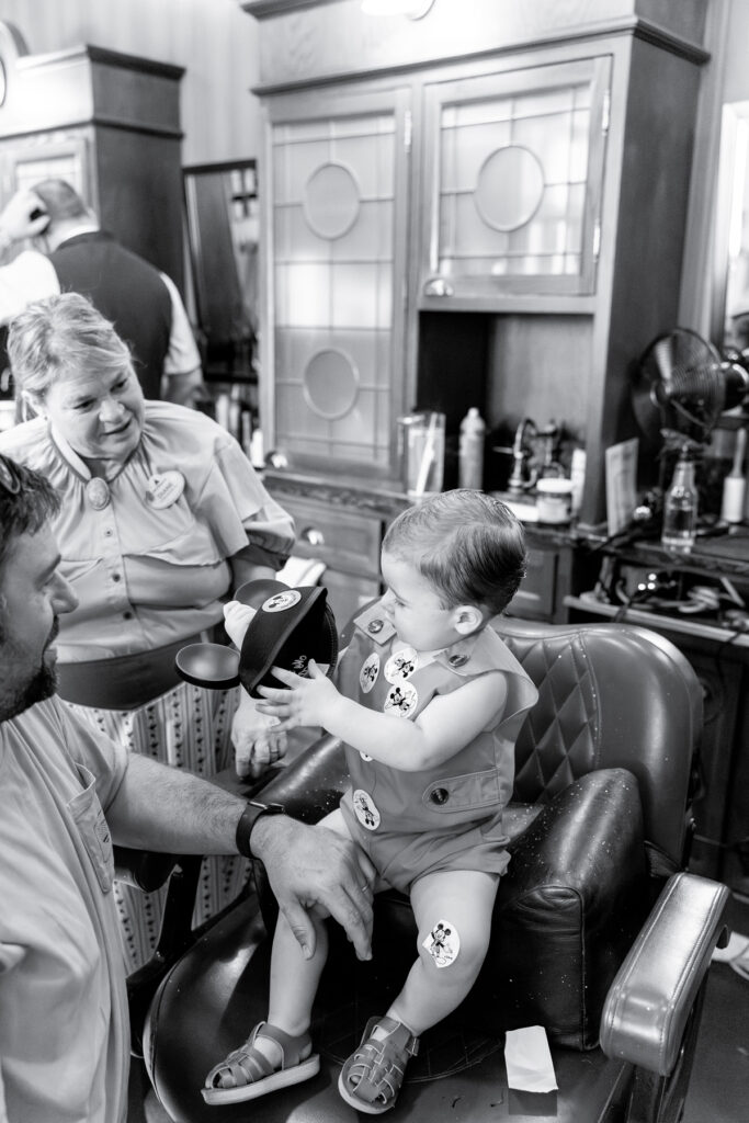 Black and white edit of a little boy in a salon chair in Disney World, looking at a new pair of Mickey Mouse ears.