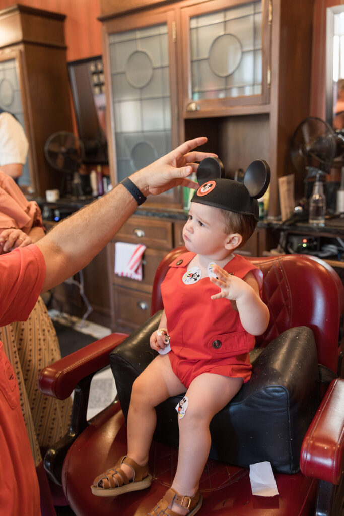 A little boy looking unsure as his dad puts a Mickey Mouse hat on his head.