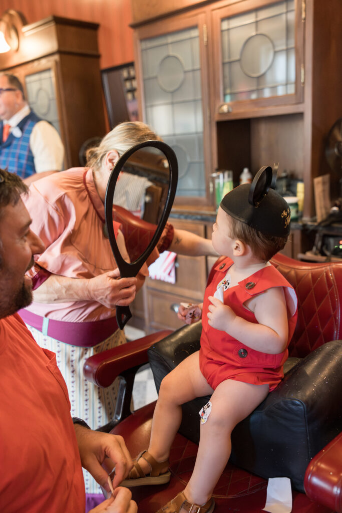 A little boy looks in the mirror after his first haircut, while his mom, a Savannah family photographer, takes pictures of him.