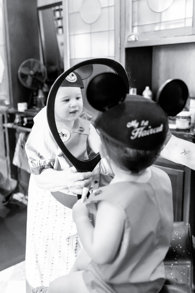 A toddler looks into a mirror at Disney's Harmony Barbershop after his first haircut which was photographed by his mother, a Savannah family photographer.