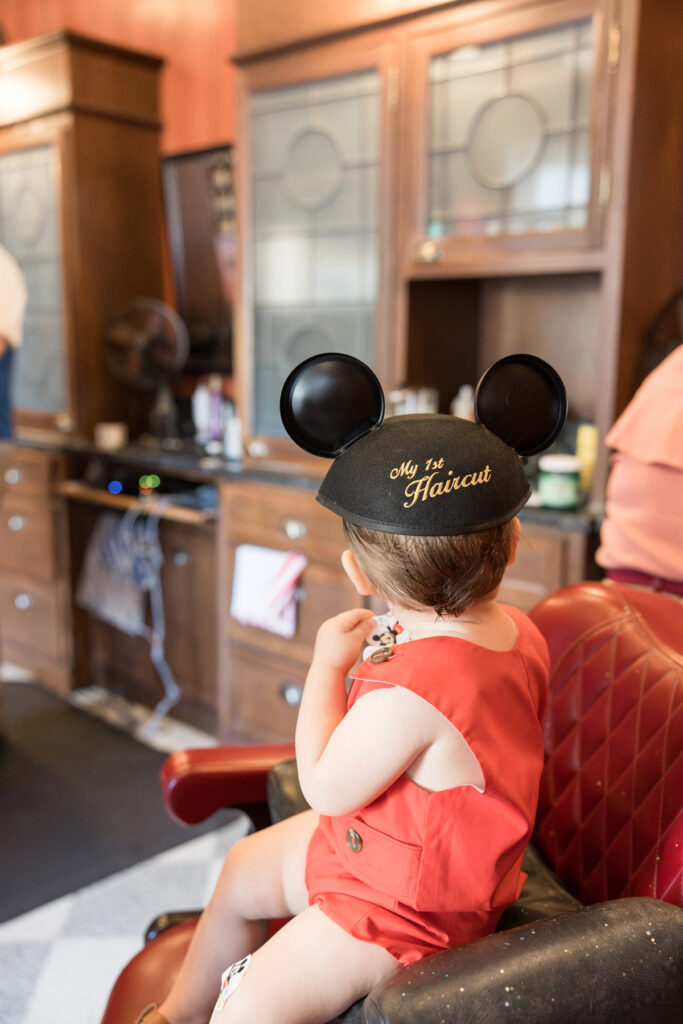 Mickey ears with "My 1st Haircut" are the focal point for this photo of a little boy sitting in a stylist's chair after his haircut.