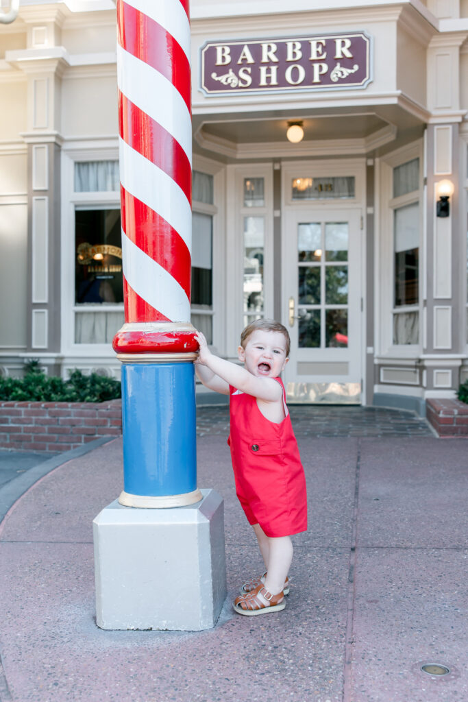 Little boy in red outfit laughing in front of Harmony Barbershop.