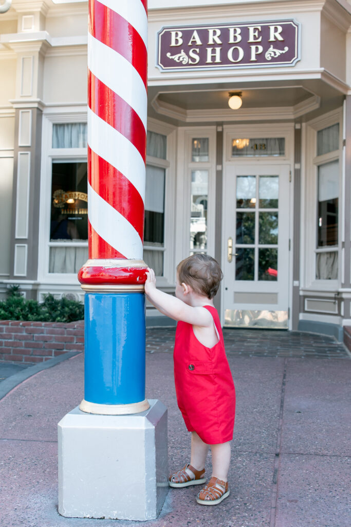 Boy in red outfit looking away from camera in front of barbershop.