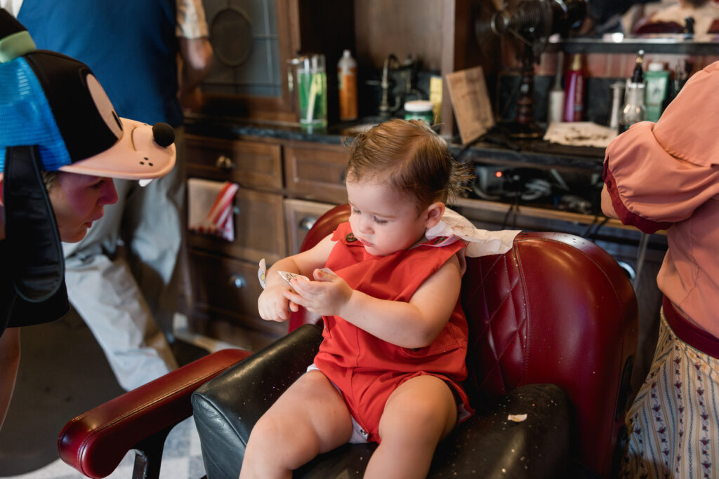 A little boy in red plays with stickers while waiting to have his first haircut.