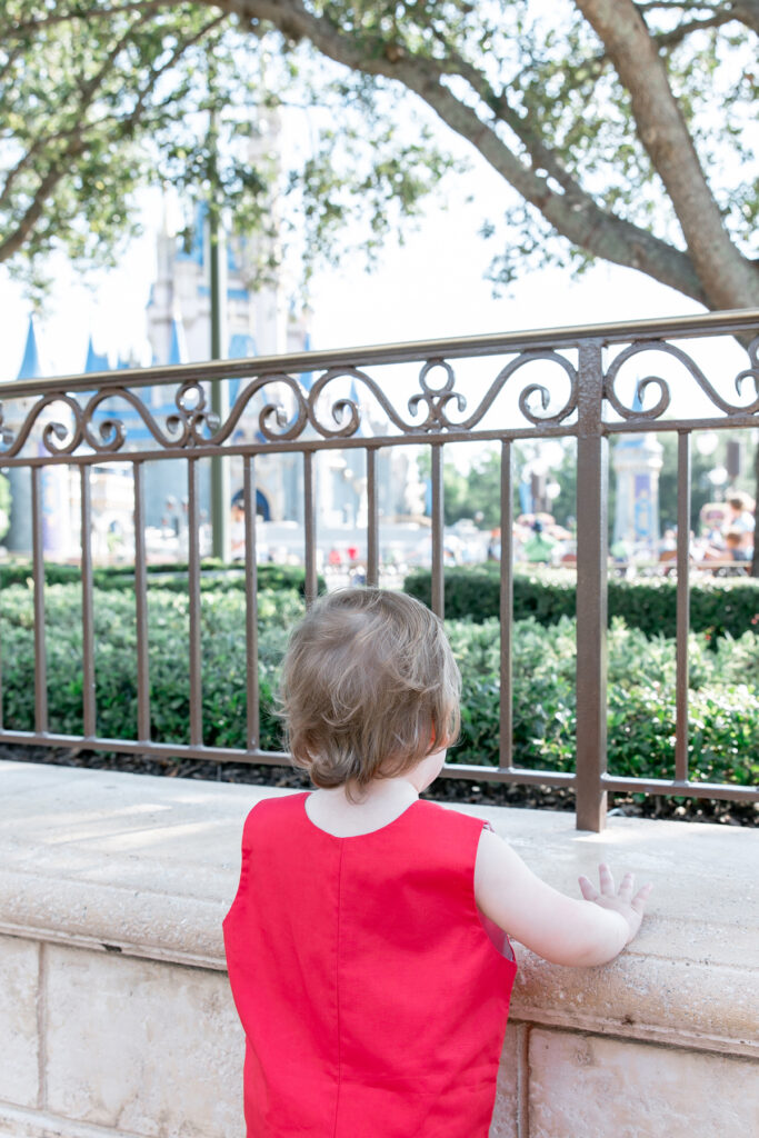 Dressed in red, Savannah family photographer Tiffany's youngest son look at Cinderella's castle before his first haircut.