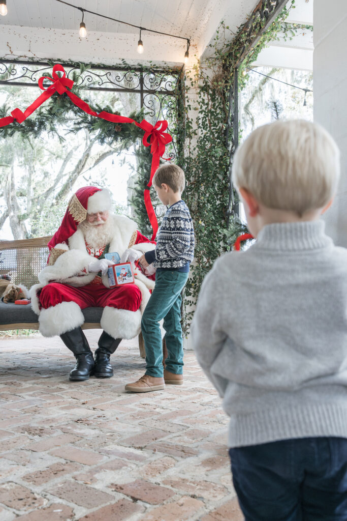 A little boy looks on as his brother plays with a jack-in-the-box with Santa during their appointment at Santa's HollyOaks Holiday.