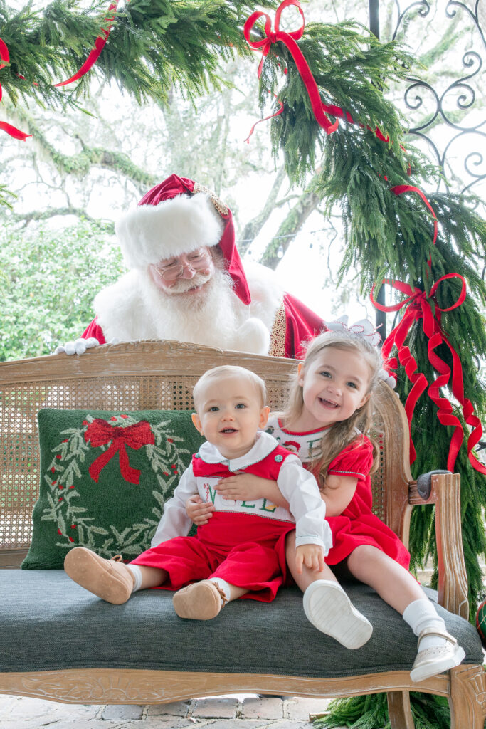 A brother and a sister sit in an area decorated for Christmas in Savannah, Georgia while Santa looks on from behind them.