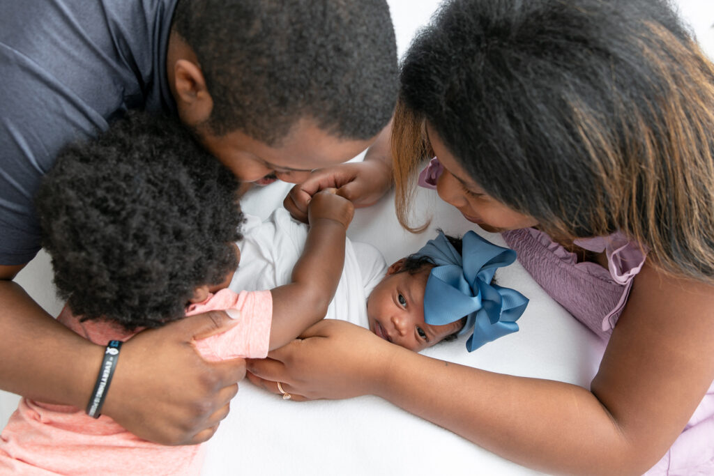 A new family of four all look and hold on to the new baby during their in-home newborn session with Savannah maternity photographer, Tiffany Bradley.