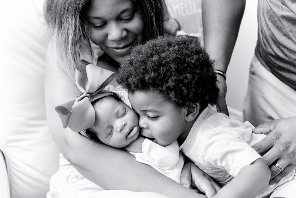 A toddler older brother kisses his new sister during their in-home newborn session.