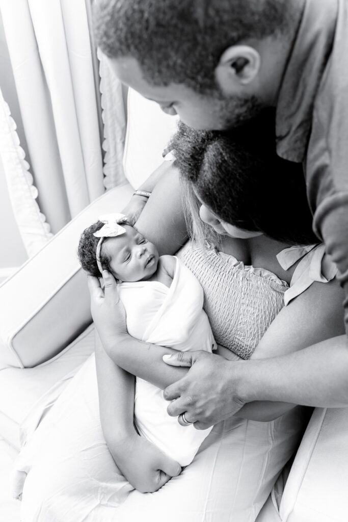 Mom, Dad, and baby snuggled together in a rocking chair by a window.