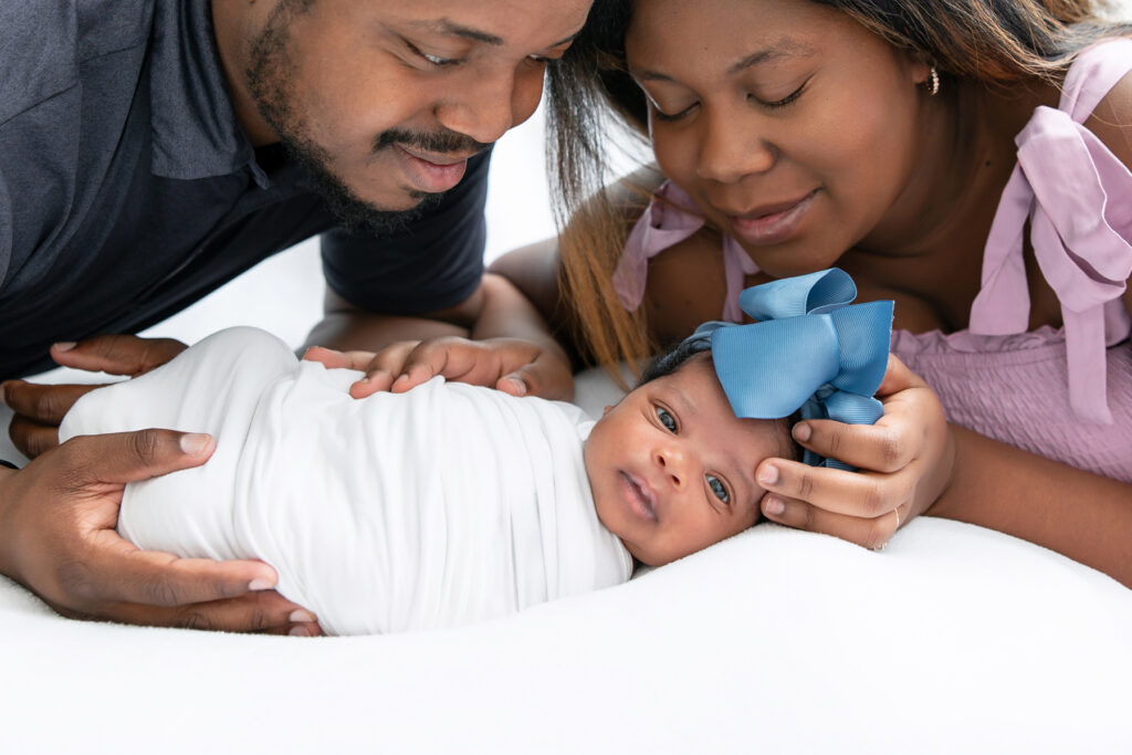 A newborn baby looks at the camera as her parents look at her during an in-home newborn photo session in Savannah, Georgia.