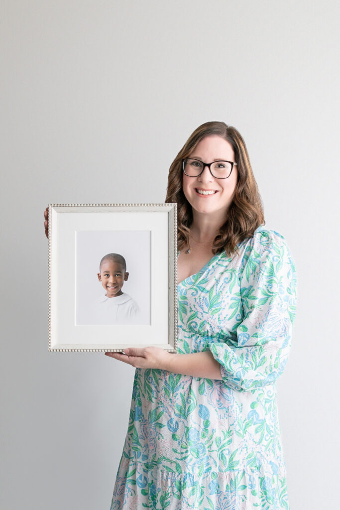 Tiffany of Tiffany Bradley Photography, a photographer in Savannah, Georgia, holding a framed, fine art print of a little boy's heirloom portrait.