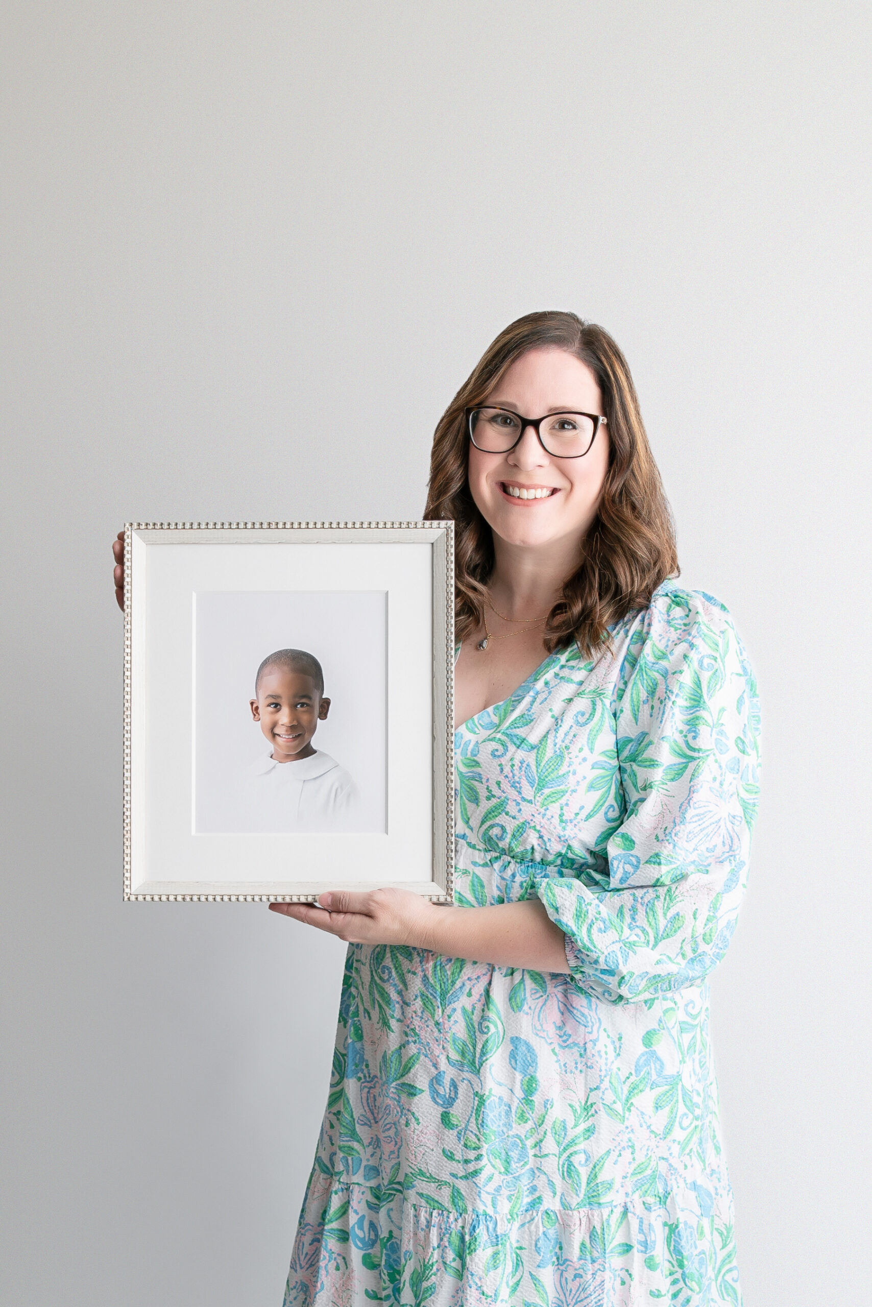 Tiffany of Tiffany Bradley Photography, a photographer in Savannah, Georgia, holding a framed, fine art print of a little boy's heirloom portrait.