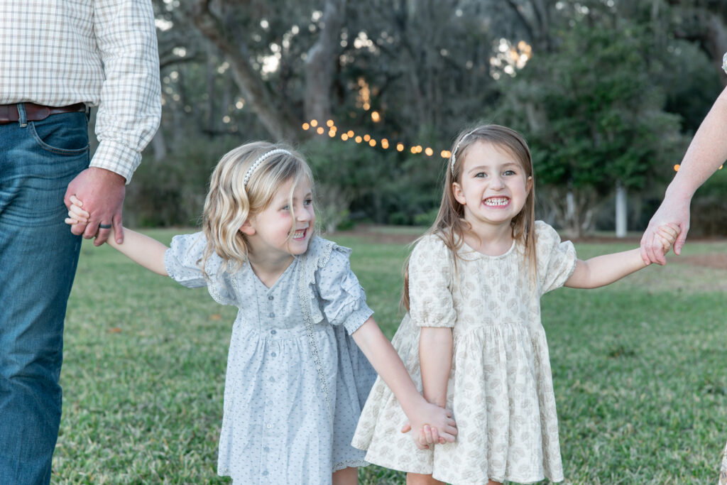 Two little girls holding hands and holding the hands of their parents, who are located off camera. 