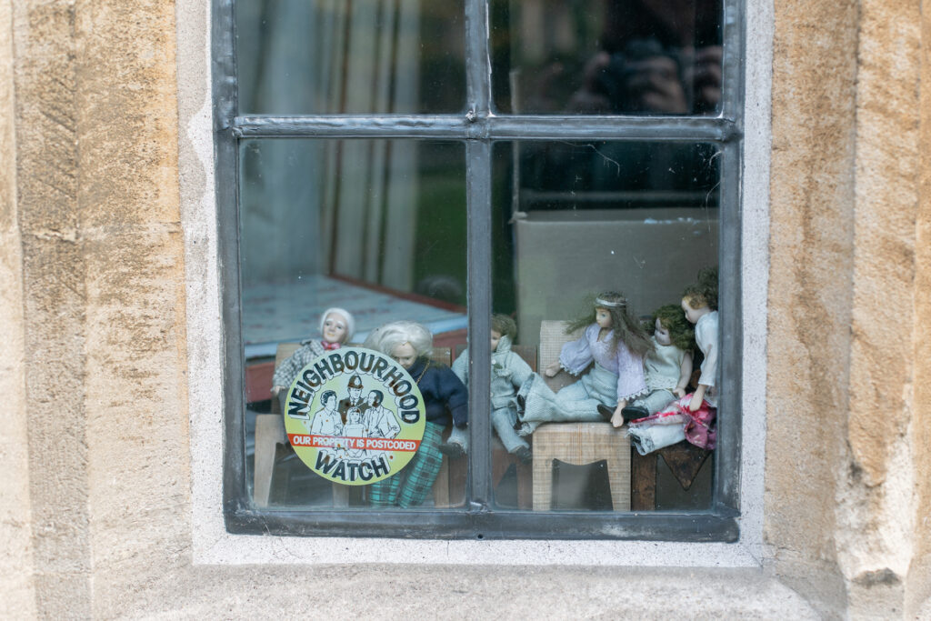 Neighborhood Watch sign with small figurines in small chairs sitting inside someone's window