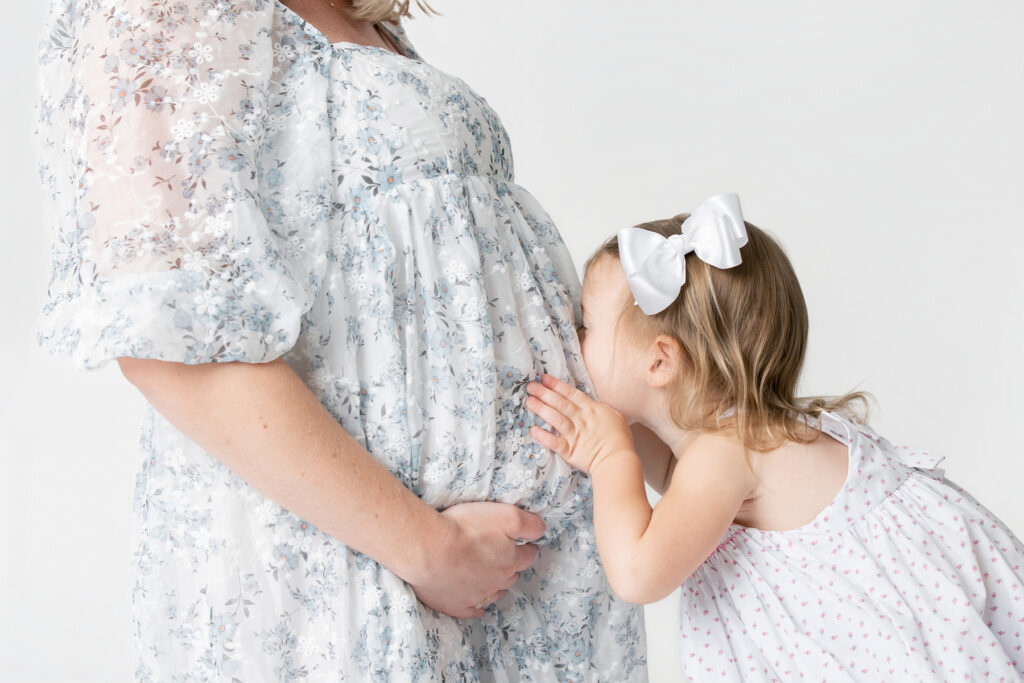 A toddler girl kisses her mom's pregnant belly during a studio maternity session Savannah.