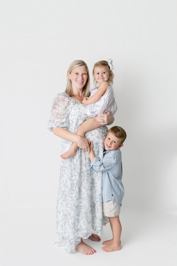 An expectant mother, pregnant with her third child, holds her daughter on her belly and her son hugs her during a studio maternity session in Savannah with Tiffany Bradley Photography.