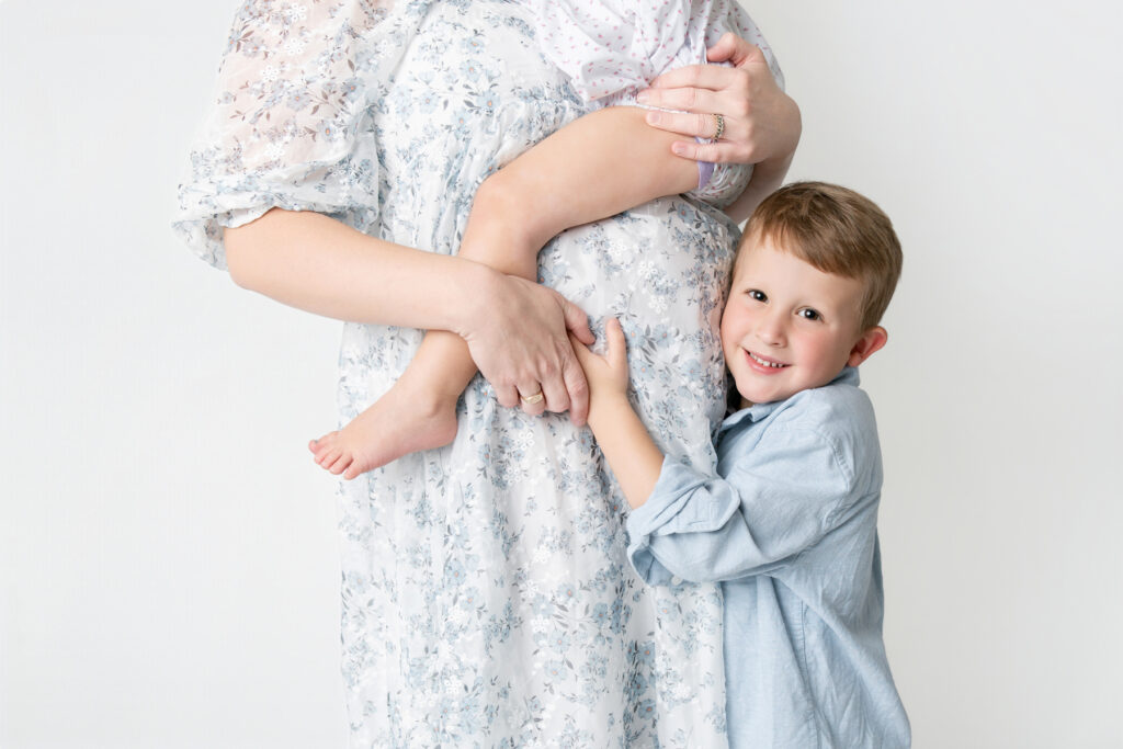 A close up of a little boy hugging his moms belly while she holds his toddler sister at a maternity photo session in Savannah.