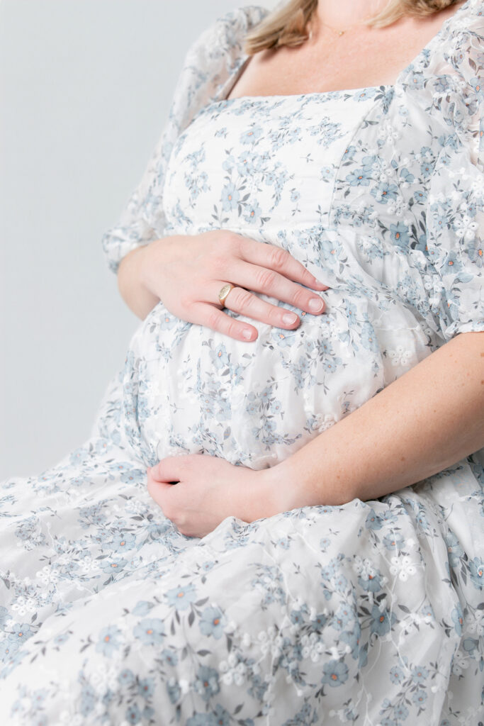 A mom holds her pregnant belly during a Savannah, GA maternity session while wearing a blue floral dress.