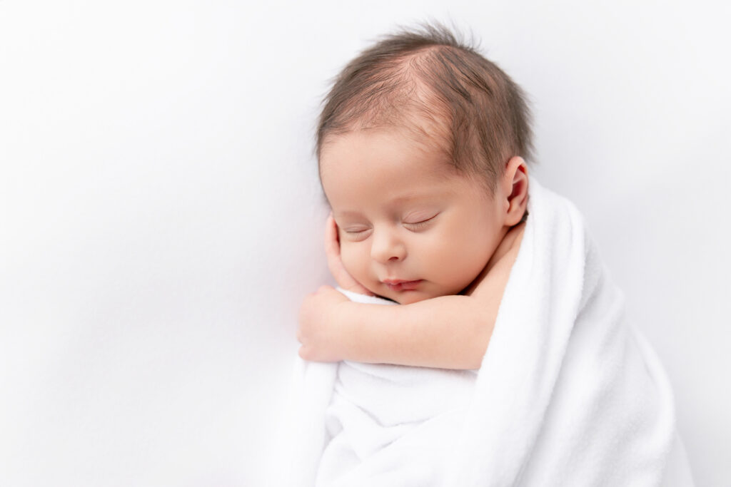 Close up photo of a newborn baby in a white swaddle on a white background at a classic newborn portrait session in Savannah, GA with Tiffany Bradley Photography.