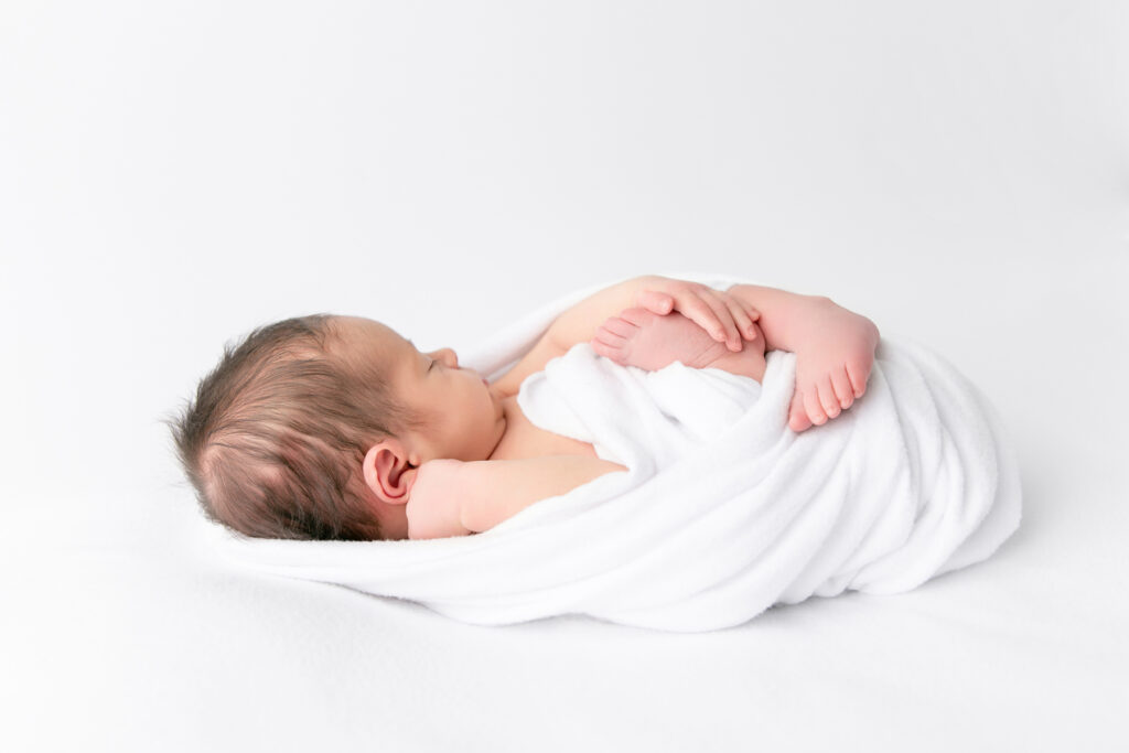 Side profile of a newborn baby boy in a white wrap on a white background.
