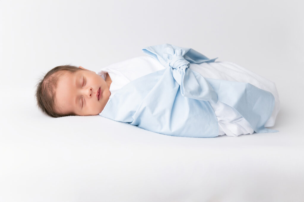 A picture of a newborn baby boy in a The Beaufort Bonnet Company blue bow swaddle, purchased from Littles on Liberty in Savannah, Georgia.