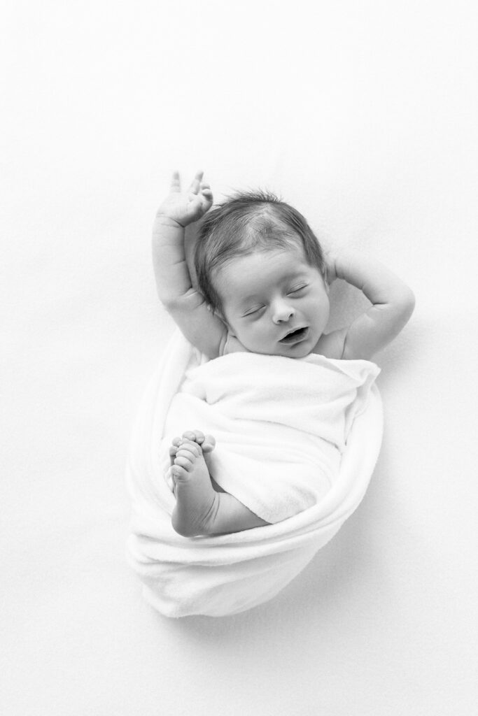A black and white portrait of a newborn baby boy mid stretch and yawn during a Savannah, Ga newborn photography session with Tiffany Bradley Photography.