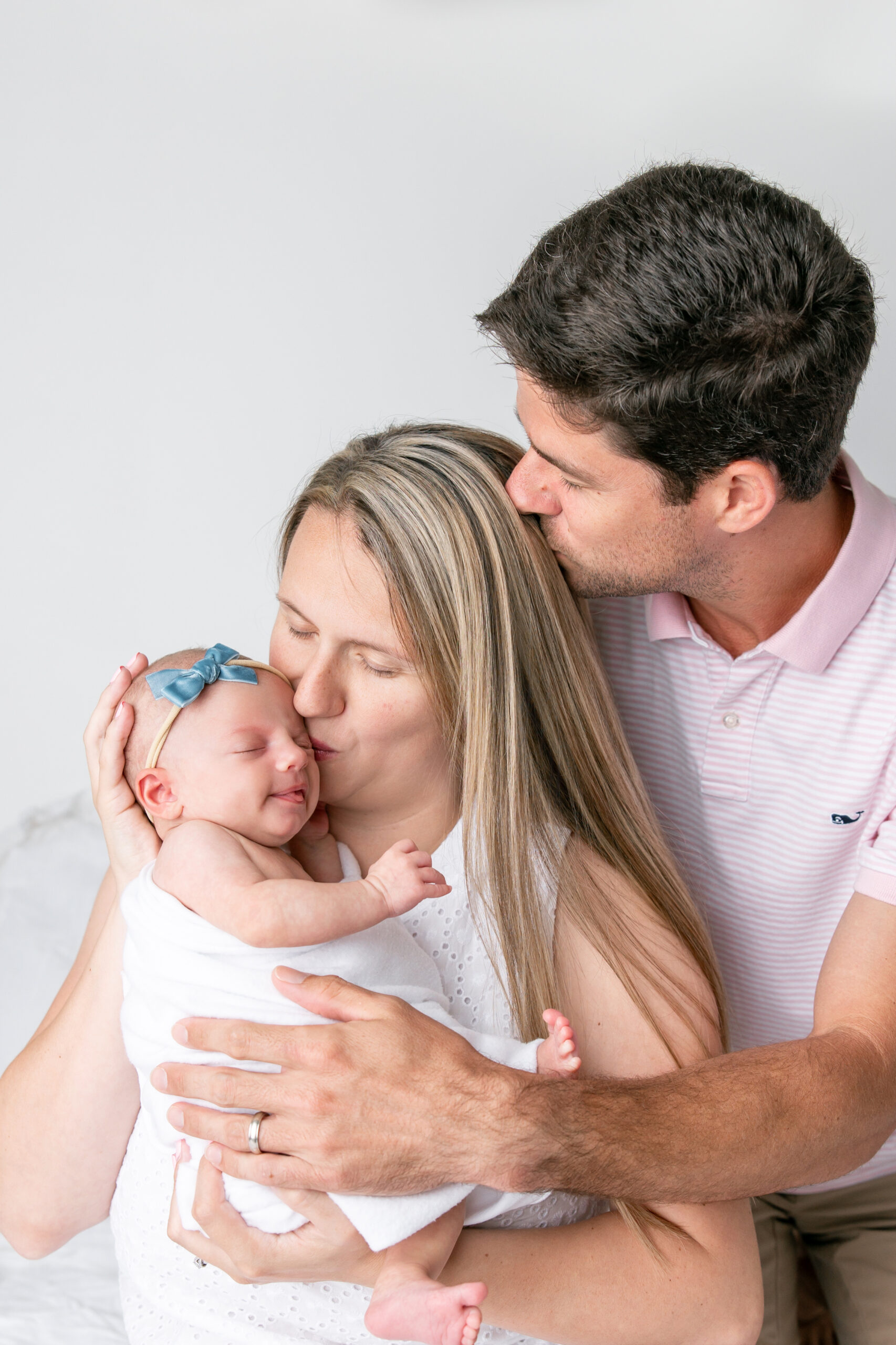 New parents kiss their newborn baby while engaging in newborn photography safety.