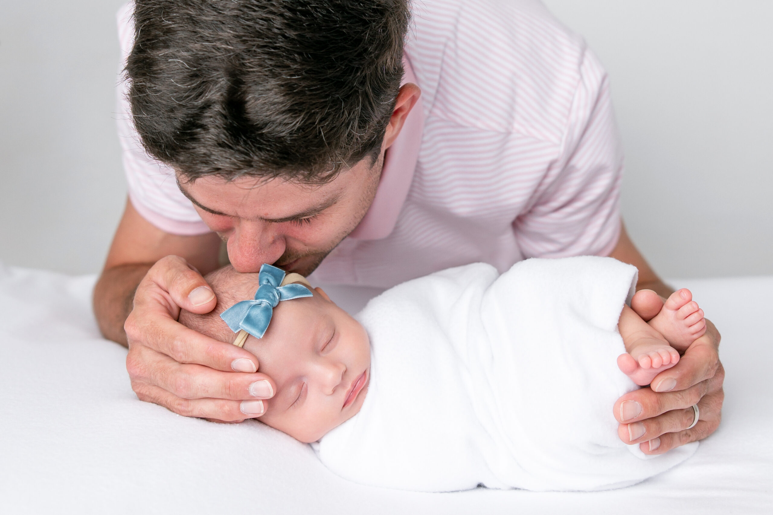 New dad kisses the newborn's head while following newborn photography safety tips from this Savannah-based photographer.