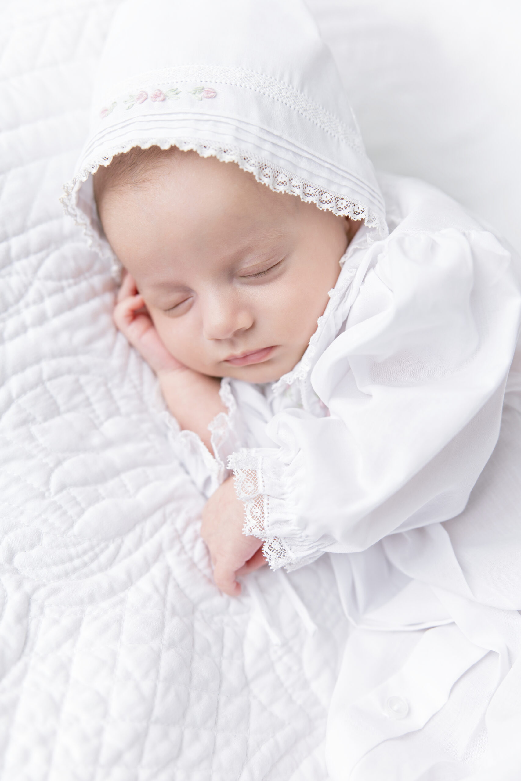 A sweet newborn in a white dress and bonnet sleeps quietly and safely as this Savannah-based photographer ensures all newborn safety tips are being followed.