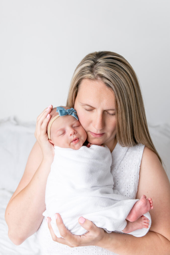 New mom follows newborn safety tips while posing with her baby, both with eyes closes, face-to-face.