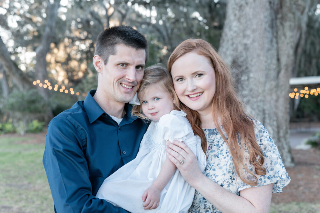 A mom, dad, and toddler daughter in front of oak trees during a fall session at HollyOaks on the Marsh with Savannah photographer Tiffany Bradley Photography.