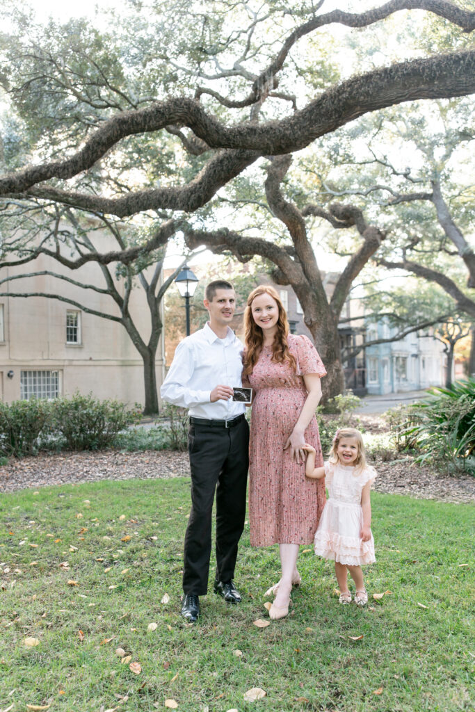 Family of three expecting their fourth baby poses in Chatham Square during a Savannah maternity pictures.