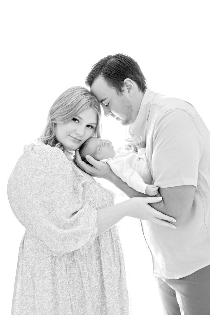 Black and white family portrait with parents and newborn baby photographed against a clean white background during a newborn photography session in Savannah, GA.