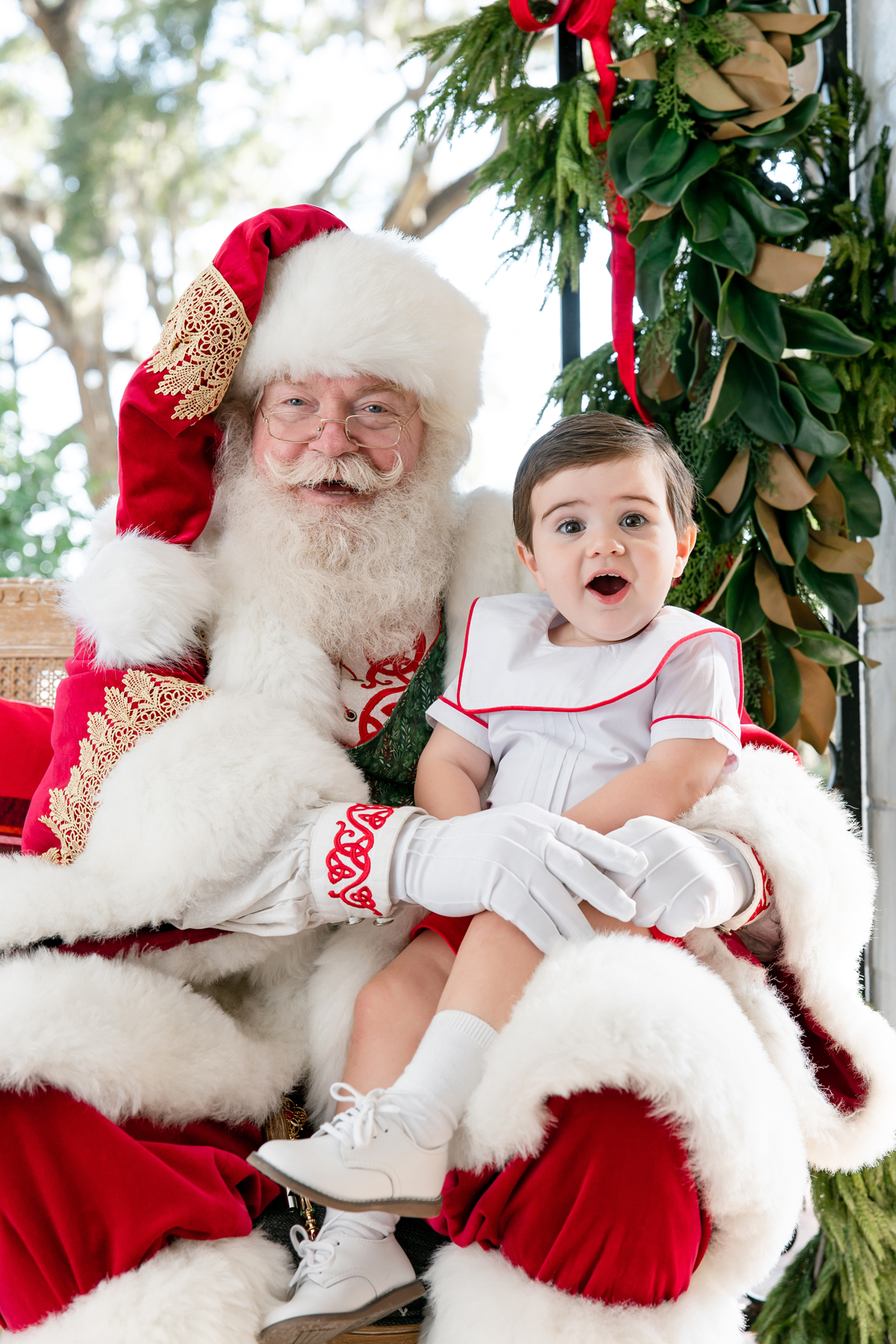 A toddler boy makes an excited face while sitting with Santa during his Savannah, GA Santa pictures.