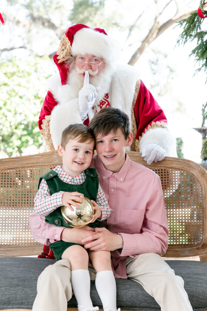 Two brothers smile while Santa peeks in on them from the background during Santa sessions in Savannah.