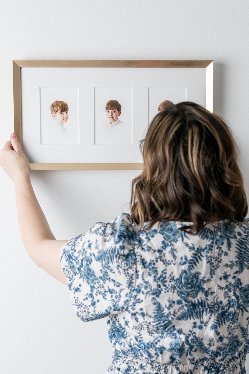 Tiffany Bradley, an heirloom portrait photographer in Savannah, GA, hangs a frame with three images from a child's heirloom portraits.