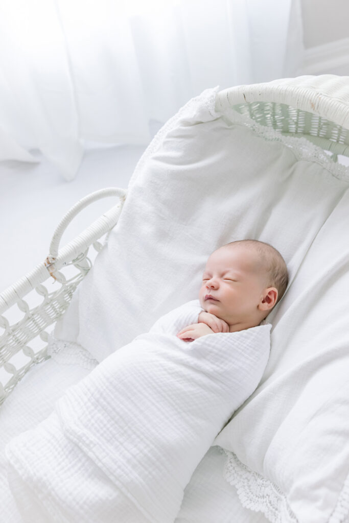 Baby swaddled in a white wrap in a Pottery Barn bassinet