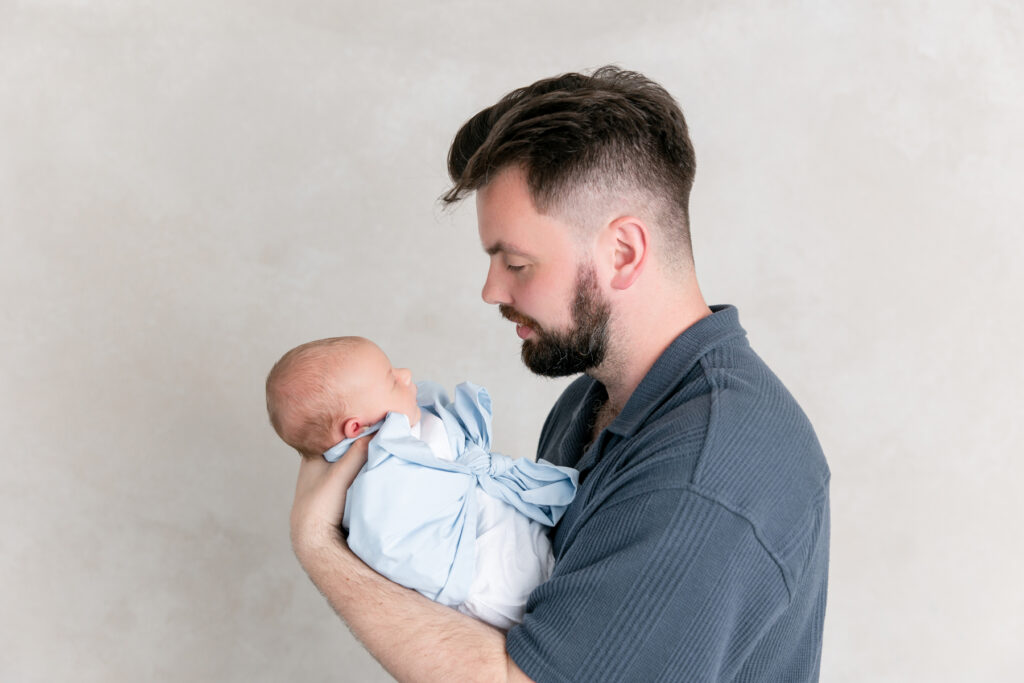 Dad holding baby, wrapped in a Beaufort Bonnet Company bow swaddle.