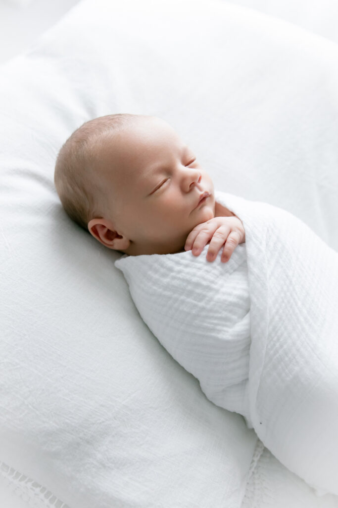 Baby, wrapped in white swaddle during in studio portrait session in Savannah.