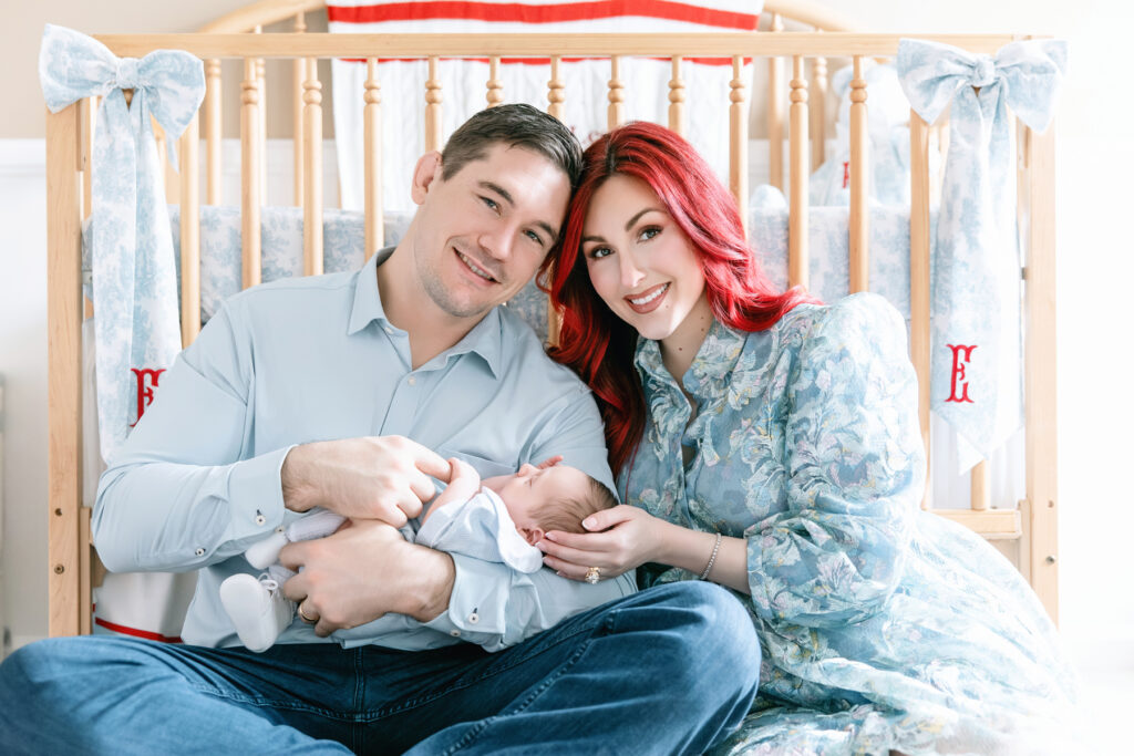 Parents with their new baby sitting in front of crib in baby's nursery.