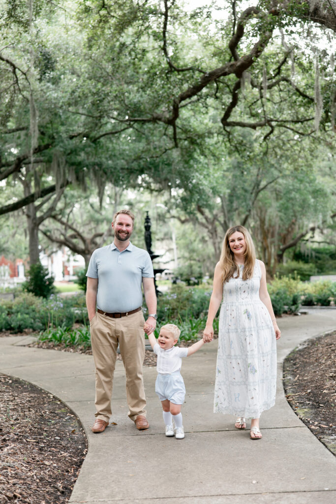 Little boy smiling while holding his mom and dad's hands walking in Savannah, GA park